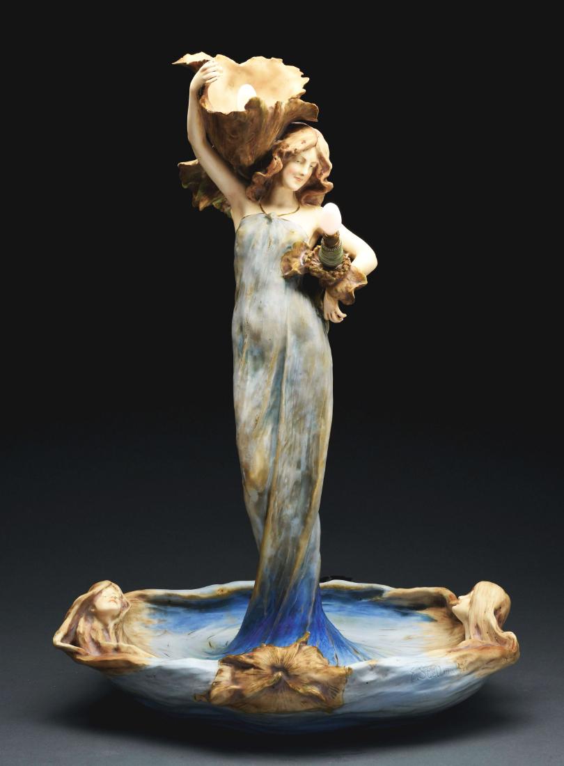Amphora Figural Lamp.: Amphora lamp has tall Art Nouveau maiden standing in water holding a large flower on her shoulder and a smaller flower with her other arm. She is wearing a long, flowing blue gown. The water forms a s