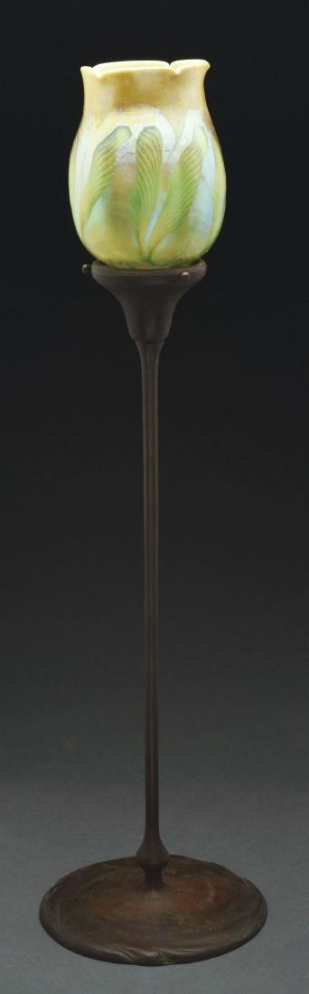 Tiffany Studios Candle Lamp.: Tiffany Studios candlestick has organic form foot with tall slender stem, leading to a simple flaring shade holder and candle cup. The candlestick is finished in a rich brown patina and supports a Tif