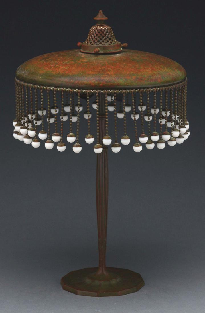 Tiffany Studios Lamp.: Tiffany Studios bronze lamp has platform foot and tall slender stem, leading to a two-socket cluster. The bronze shade is supported by an acid-etched bronze holder. The shade supports beaded chains, f