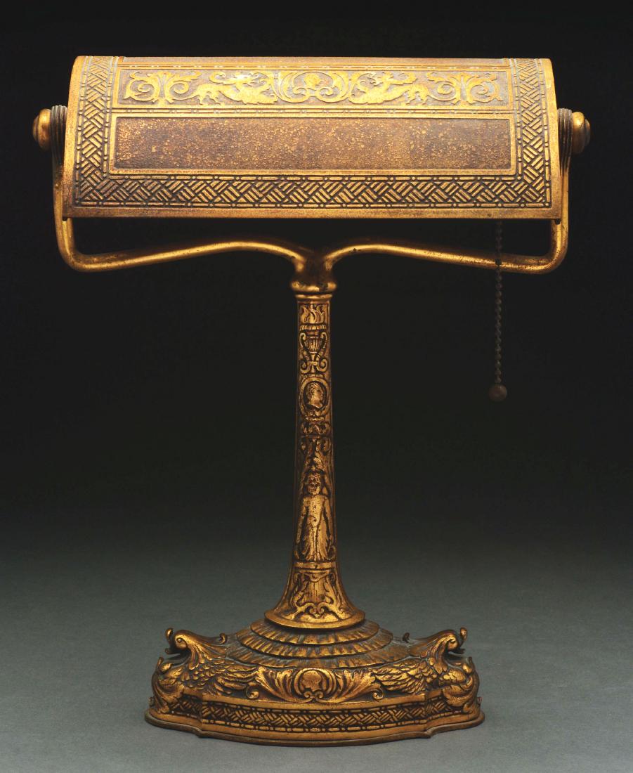 Tiffany Studios Spanish Desk Lamp.: Tiffany Studios bronze desk lamp in the Spanish pattern has flying dolphin heads on each side of the base and ornate scroll work decorating the stem. The wide shade is decorated with a central panel w