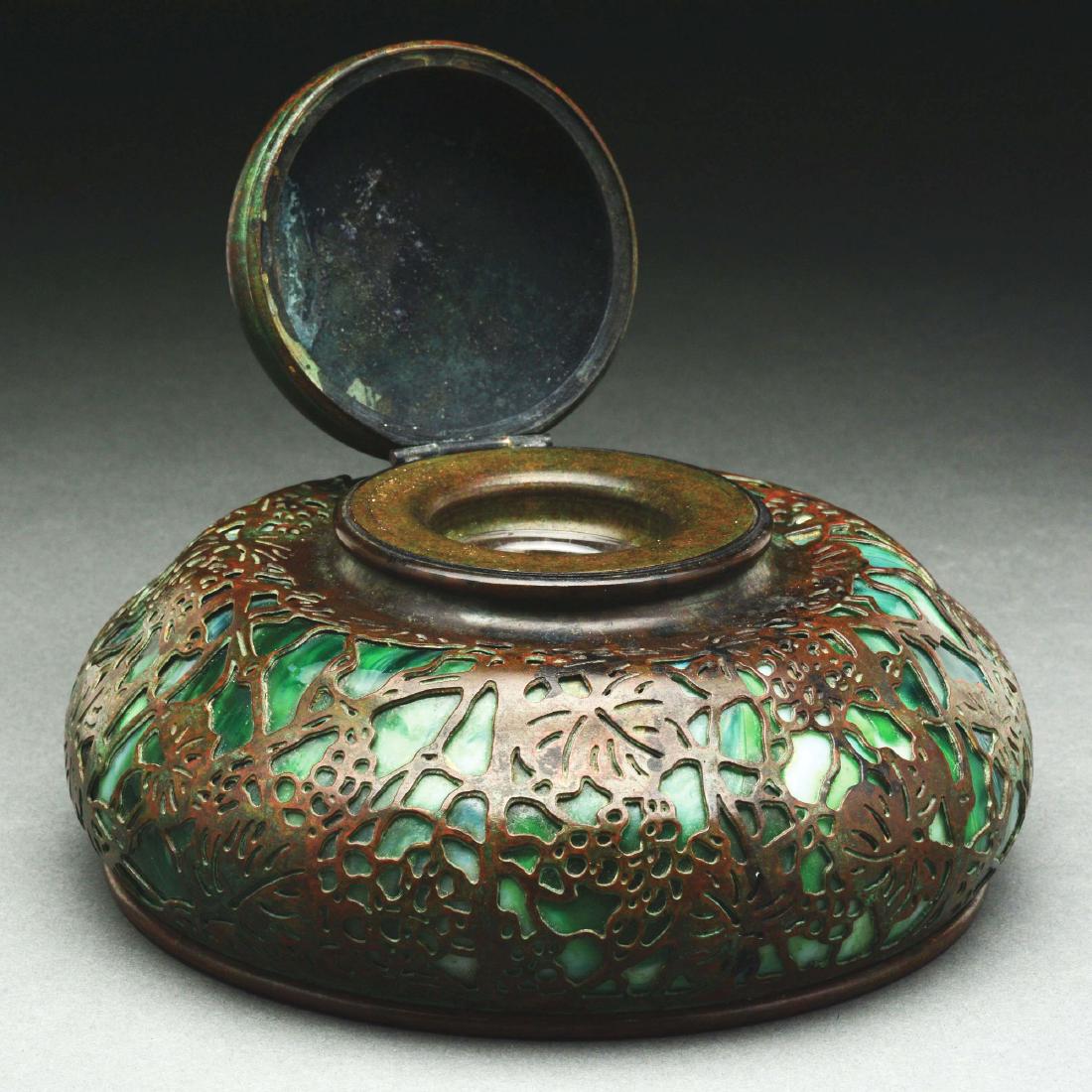 Tiffany Studios Grapevine Inkwell.: Tiffany Studios bronze inkwell has acid-etched grapevine design with green slag glass backing. The bronze is finished in a rich brown patina. Inkwell retains a glass insert. Marked on the underside "T