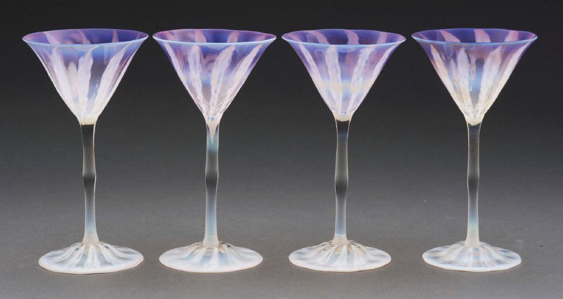 Four Tiffany Favrile Pastel Cordials.: Tiffany Favrile pastel cordials have clear, slender stem and inverted saucer foot with white, lightly opalescent ribbons against a clear background. The cordial cup is pastel purple with vertical band