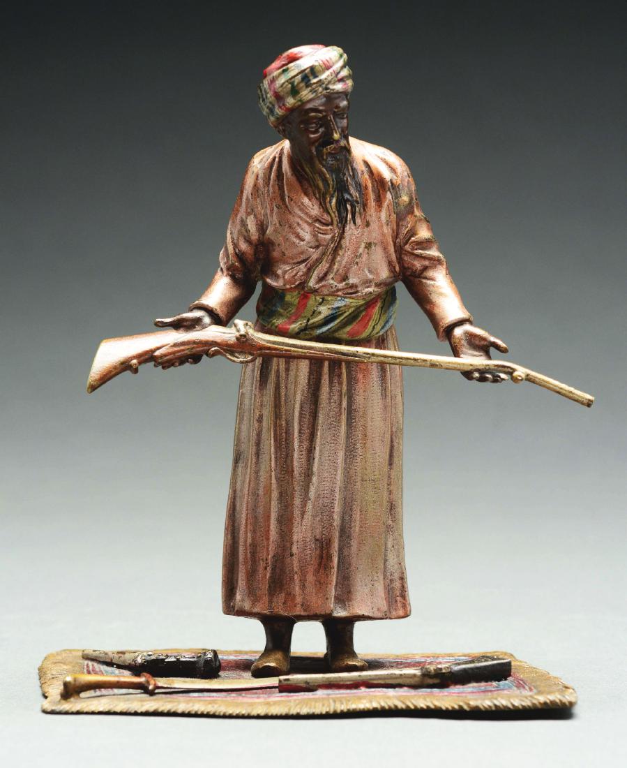 Austrian Bronze of Man Holding Gun & Three Weapons on: Statue depicts an Arab man proffering a rifle as he stands on a rug with a sword and two pistols at his feet. The metal has colored areas. This excellent condition 6" tall bronze figure does not appea