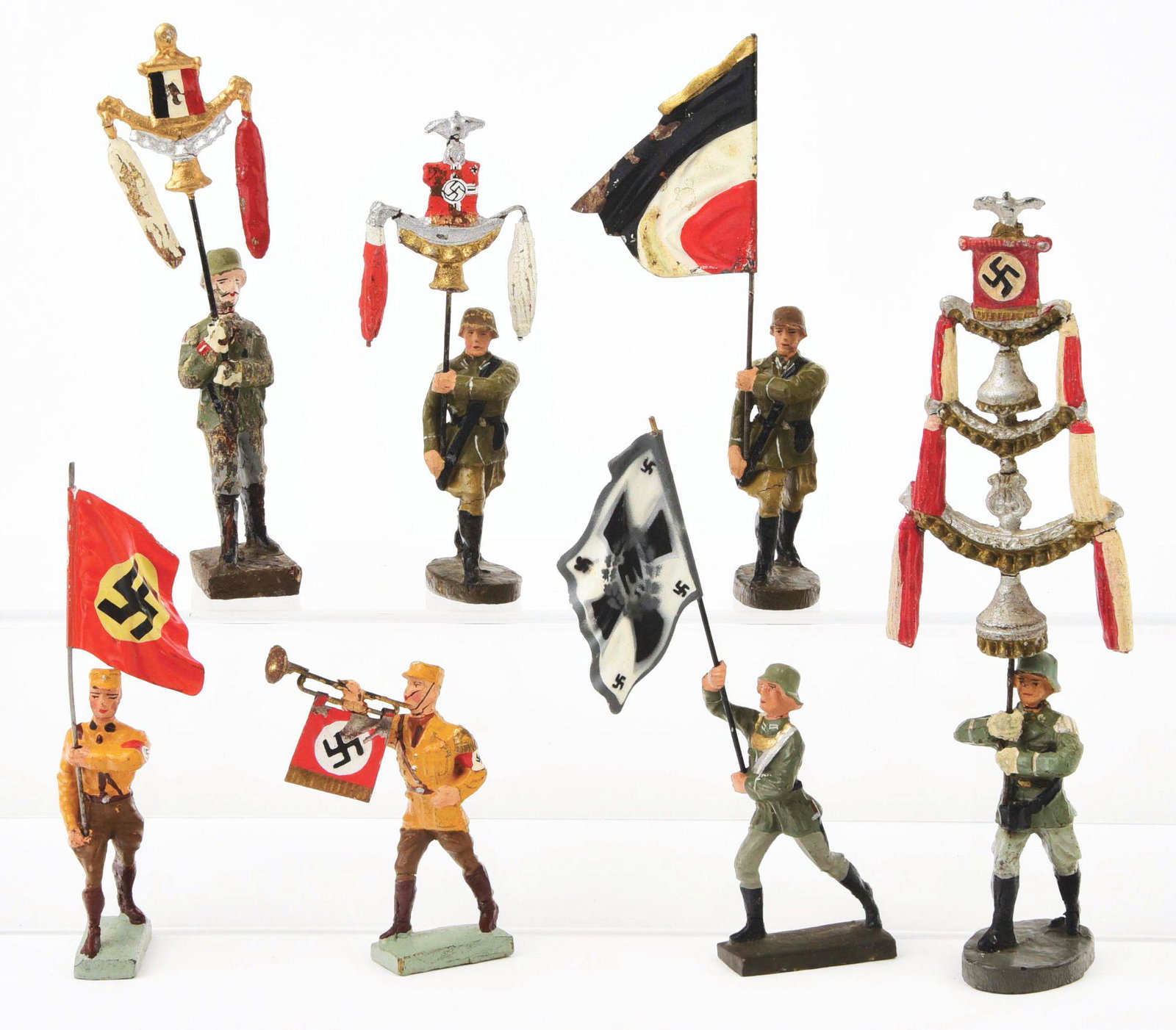 LOT OF 7: VARIOUS ELASTALINE AND LINEOL COMPOSITION: Includes Brown Shirt blowing trumpet with tin Nazi sign, a Nazi flag-bearer with red flag and Nazi insignia, a Nazi flag-bearer with grey and white Nazi flag with four small Nazi insignia on corners a