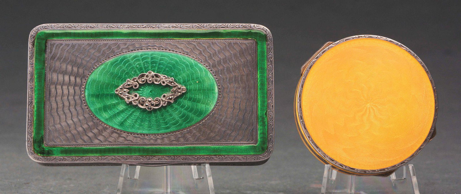 LOT OF TWO ENAMELED COMPACTS.: Lot consists of: first, a rectangular silver compact with a stylized leaf design surrounding the sides, along with machine turning on the top, with green enameled center oval, finished with a silver f