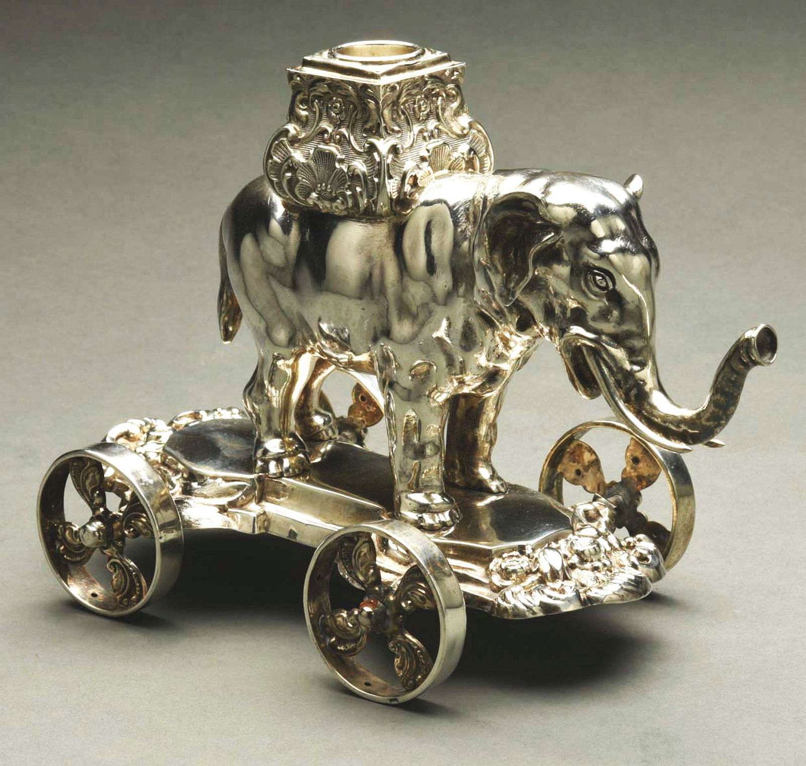 A SILVER ELEPHANT TABLE ORNAMENT.: Modelled standing with a scroll-chased howdah on its back and on a shaped base with molded edges and four wheels. Indistinct marks; with French import mark. Repair to area of mark. Height: 6 - 7/8" We