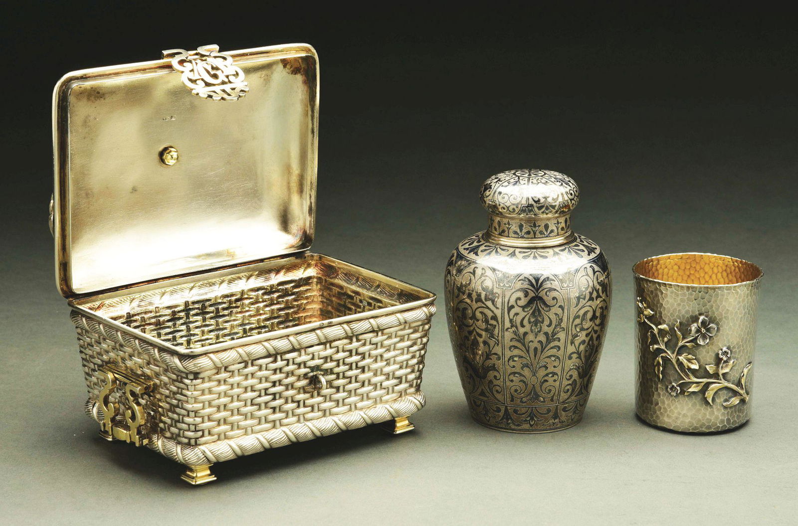 A RUSSIAN FIGURAL SILVER CASKET.: Moscow 1887. Chased as a wicker basket with napkins on the flat lid, the hinged handles and hasp pierced and gilt; together with a beaker, St Petersburg 1884, with hammered finish and chased with a fl