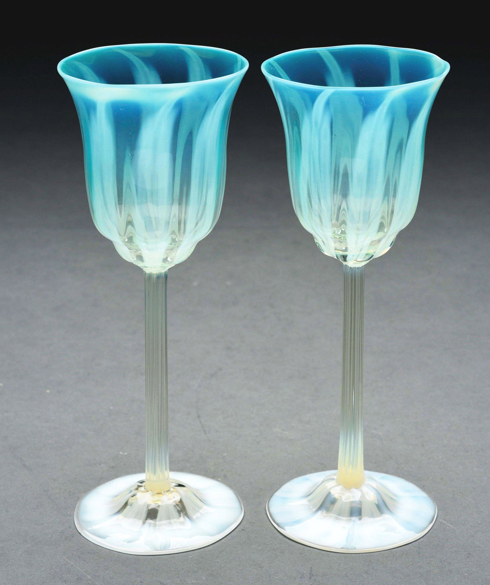 LOT OF 2: TIFFANY FAVRILE PASTEL WINES.: Lot consists of two matching Tiffany pastel wines, each with inverted saucer foot with ribbons of opalescence. The vertically ribbed stems lead to pale blue-green pastel bowls with vertical ribbons of