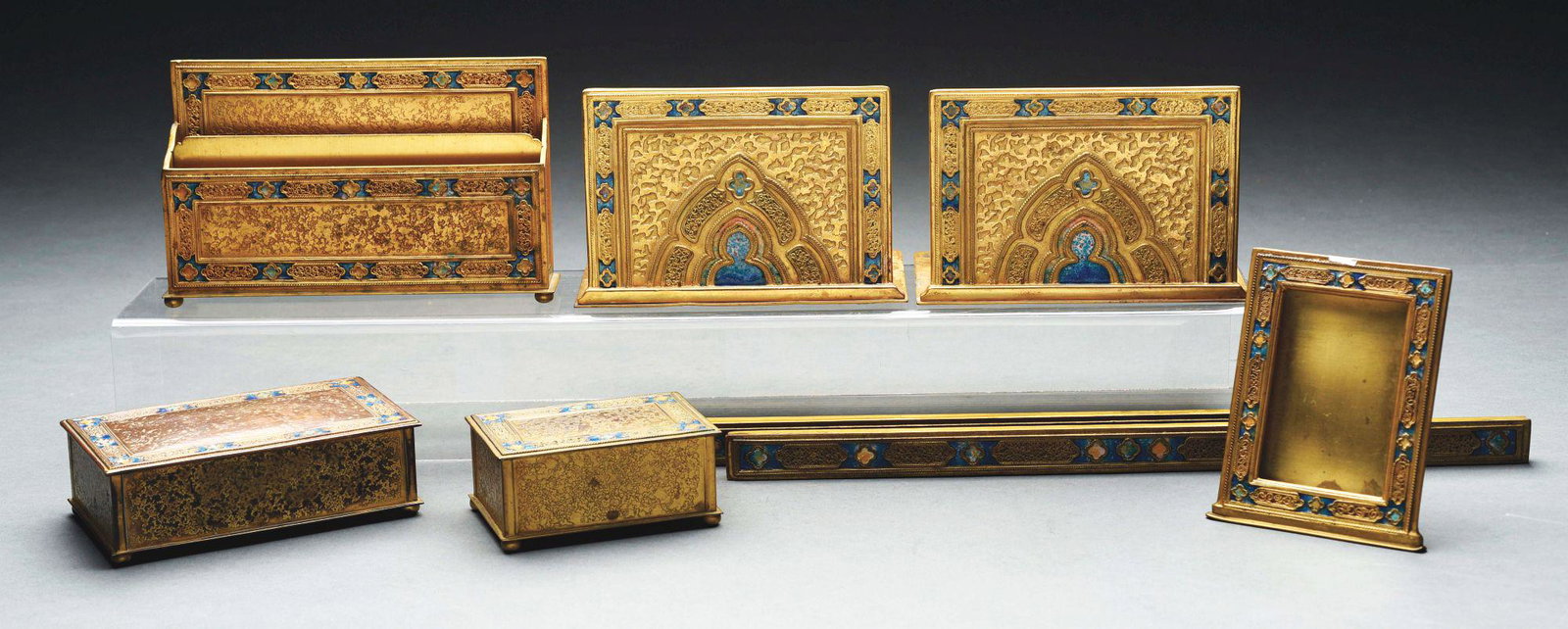 TIFFANY DOUBLE XX ENAMELED DESK SET.: A rare Tiffany Studios five piece gilt bronze and enameled "Double XX" pattern desk set by Louis C. Tiffany Furnaces compromising of a picture frame, letter rack, blotter ends, cigarette box, and a ut
