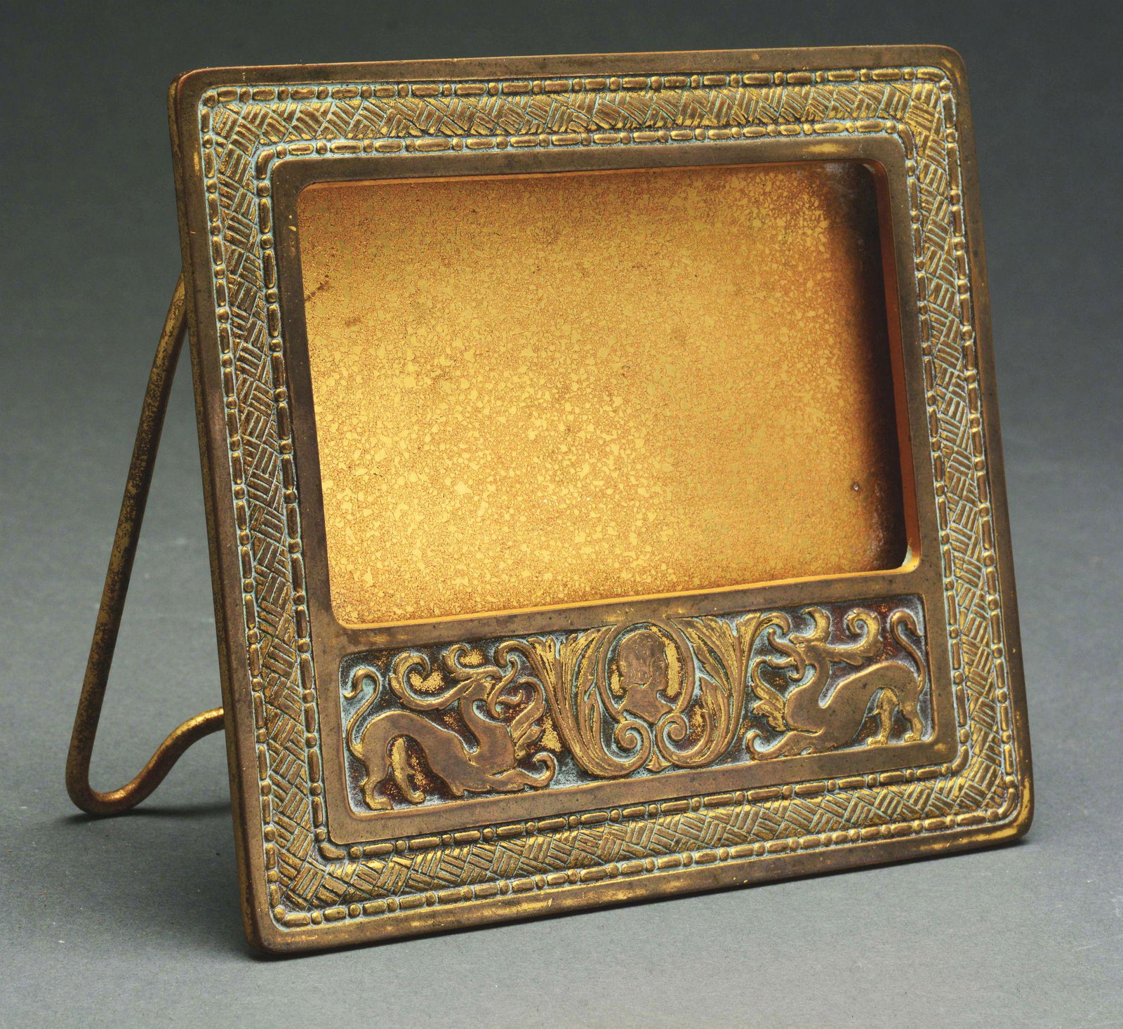 TIFFANY STUDIOS SPANISH CALENDAR FRAME.: Tiffany Studios bronze calendar frame is done in the Spanish pattern with ornate decorations, scrolls and mythical beasts surrounding the bust of a man. The frame is finished in a gold patina and show