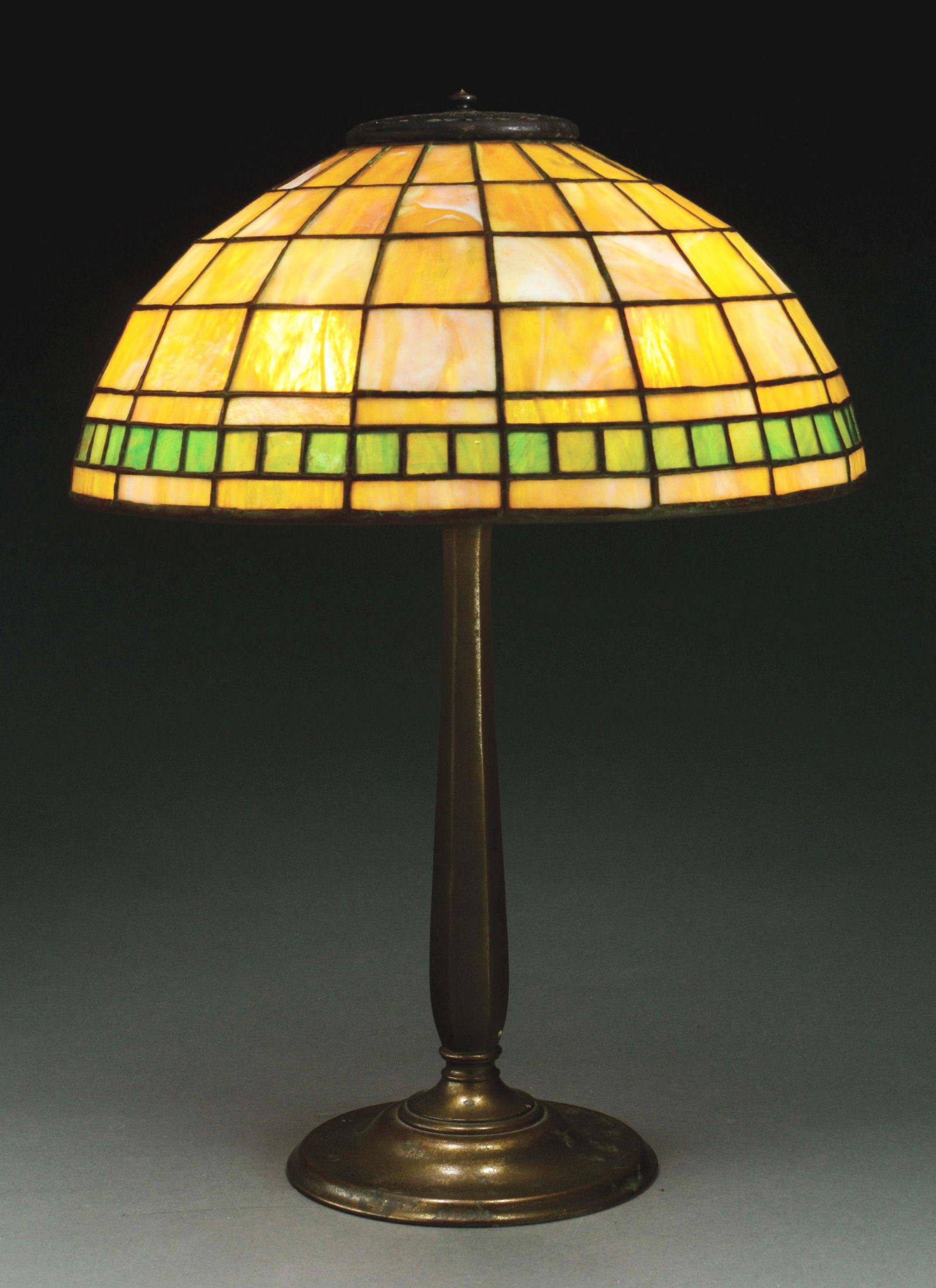 TIFFANY STUDIOS COLONIAL TABLE LAMP.: Tiffany Studios table lamp has leaded glass shade in the colonial pattern with a single band of square green panels surrounding the bottom of the shade against a caramel and cream geometric background