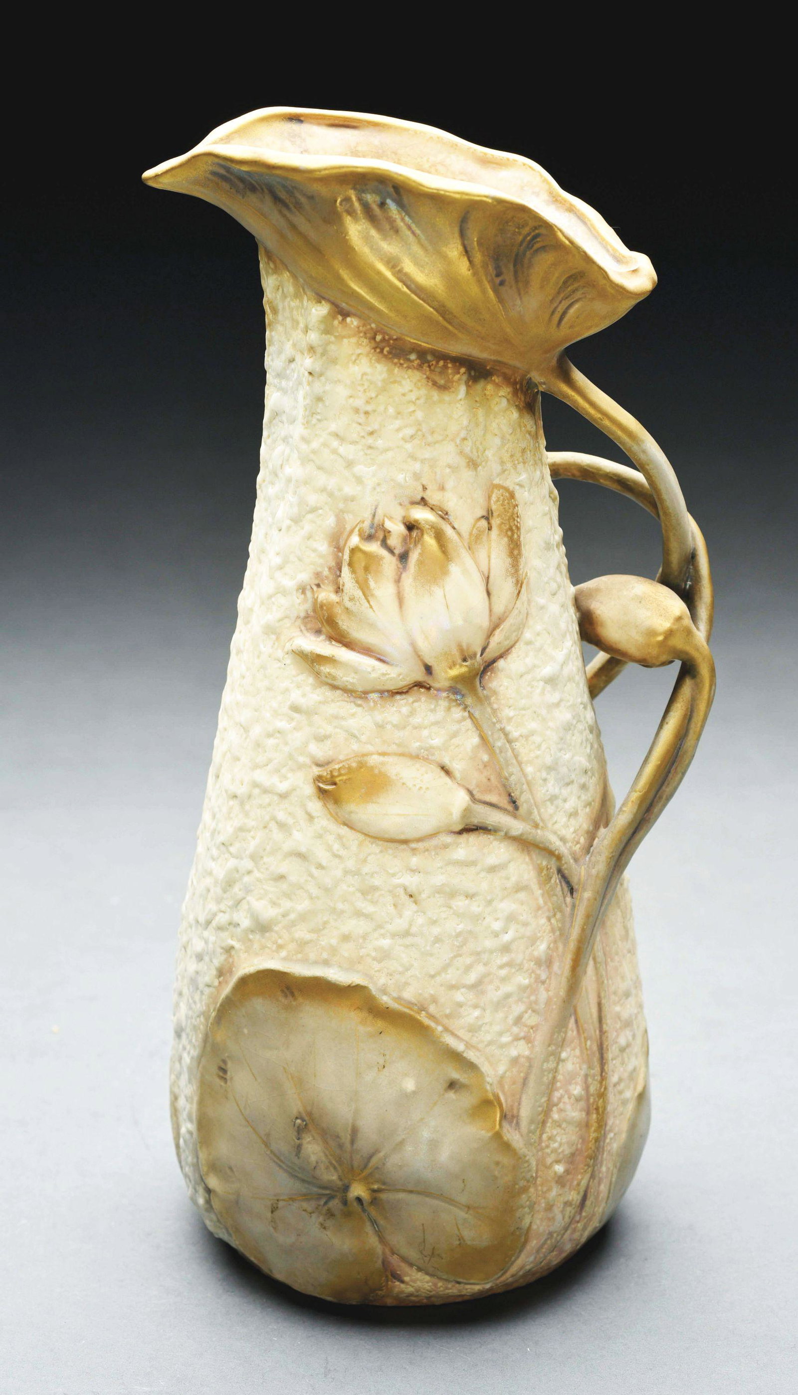 AMPHORA PITCHER WITH RAISED FLOWERS.: Intricate applied floral handle and raised flowers on the pitcher. Gold and cream glazes. Crown mark, Amphora Oval mark, Austria Oval mark, impressed “5360-44”. 12 - 1/4" high. Illustrated in "Mon