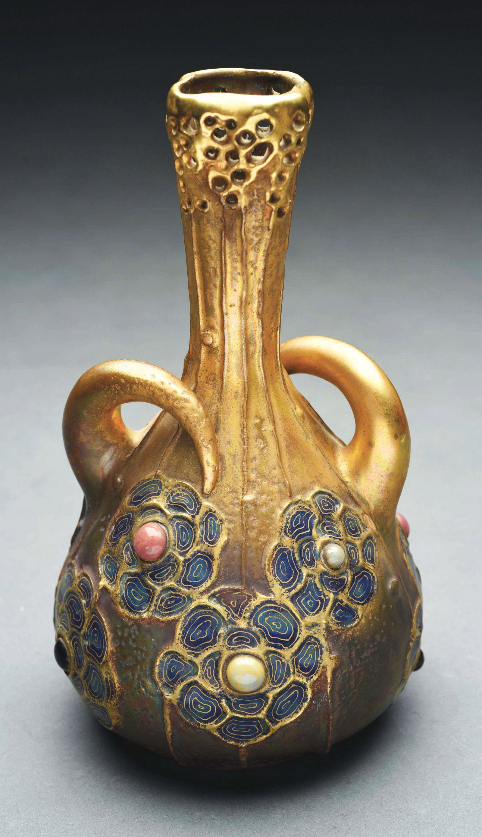 AMPHORA GRES BIJOU VASE WITH TWO HANDLES.: Iridized glazes with reticulated top, two applied handles and enameled flowers with inset jewels. Amphora Crown mark, Austria Oval Mark, RSTK Monogram, Impressed “3354-20”. 9 - 1/4" high. Illustra
