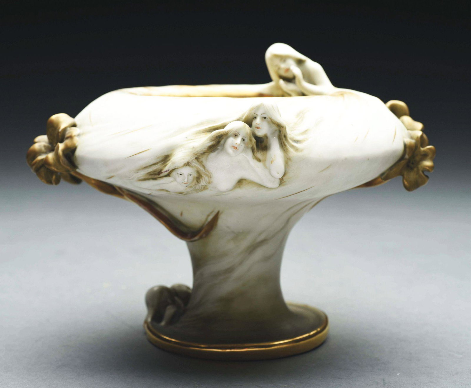 AMPHORA FATES FOOTED VASE.: Applied flowers and Fates in relief swirling around the vase. Cream glazes with gold gilt. Raised Amphora mark, RSTK mark, impressed "2007-41". 6 - 1/2" high. An example illustrated in "The House of A