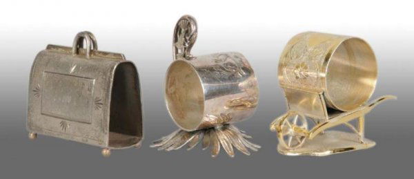 Lot of 3: Figural Napkin Rings.: Description Includes a suitcase or a valise-shaped napkin holder numbered "262" with no manufacturer's name. Next is a napkin holder with fretwork handle on palm leaves base with no manufacturer's nam