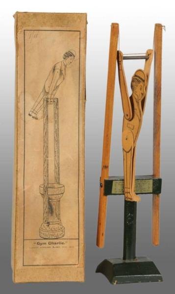 Wood "Gym Charlie" Chaplin Mechanical Toy.: Description With box. English. Patent applied for April 1919, made by W.R. and Company Ltd. Very rare. Chaplin image is printed on flat wood surface in black. Toy is operated by squeezing wooden posts