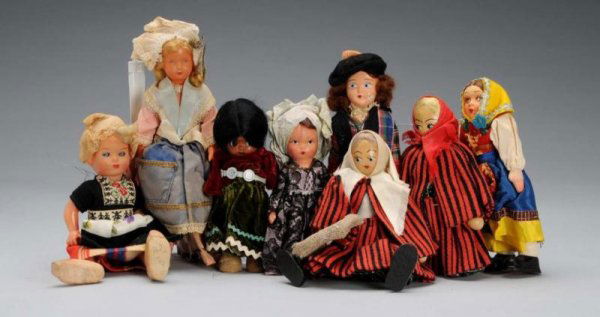 Lot of 8: Small Dolls.: Description Circa 1940 to 1950. Eight dolls in original clothes, including two woods, one celluloid, one cloth, three hard plastic, and one painted bisque. Some soiling. Condition (Good). Size Largest