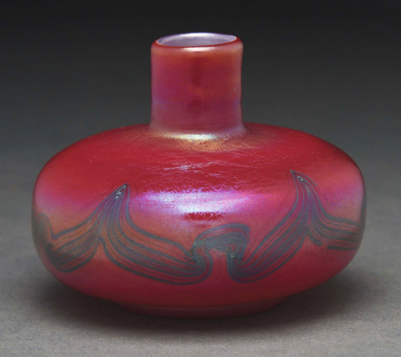 TIFFANY STUDIOS SMALL DECORATED VASE.: A small, red decorated vase by Tiffany Studios. The vase features a bulbous body with short neck. The vase is a deep cranberry with subtle iridescence, with a decorated band of purple lines across the
