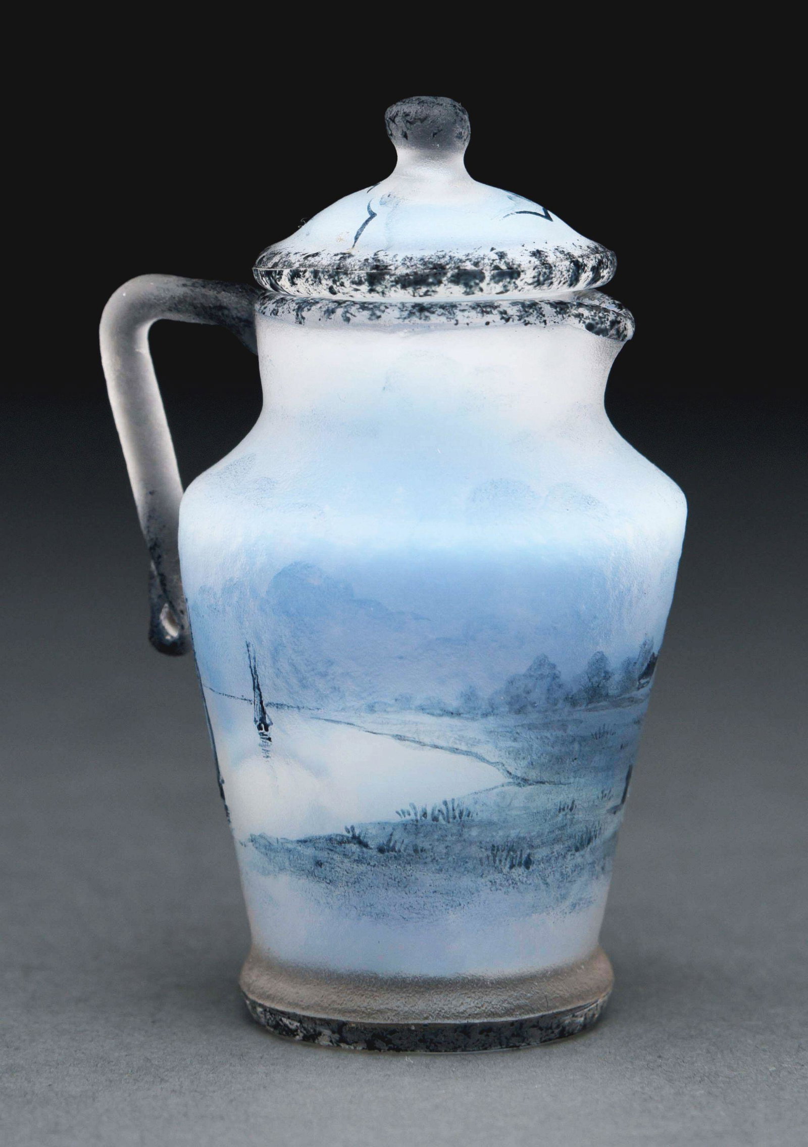 MINIATURE DAUM NANCY PITCHER WITH COVER.: A miniature pitcher with lid by Daum Nancy. The pitcher features a single handle, and depicts a Dutch scene en grisaille, comprised of windmills, lake, and sailboats, all represented in blue, set agai