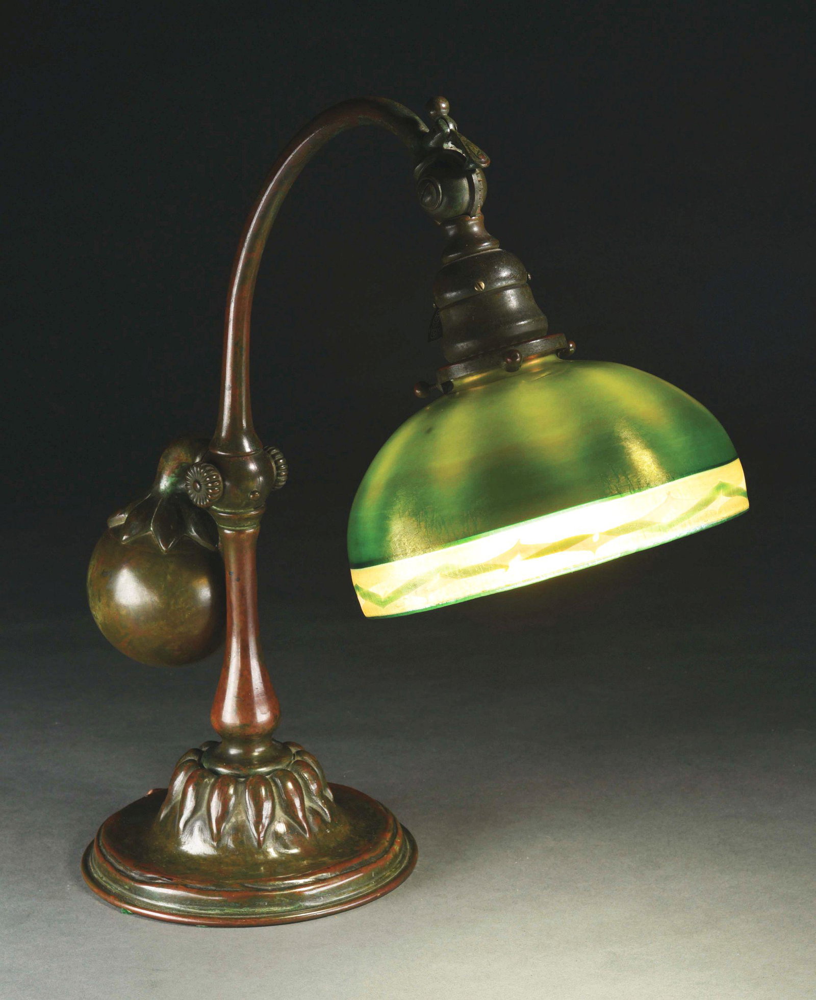 TIFFANY STUDIOS FAVRILE GLASS COUNTERBALANCE DESK LAMP.: A beautiful counterbalance desk lamp with favrile glass shade by Tiffany Studios. The 7” diameter shade is composed of beautiful green glass with subtle iridescence and gold shimmer. Above the lower