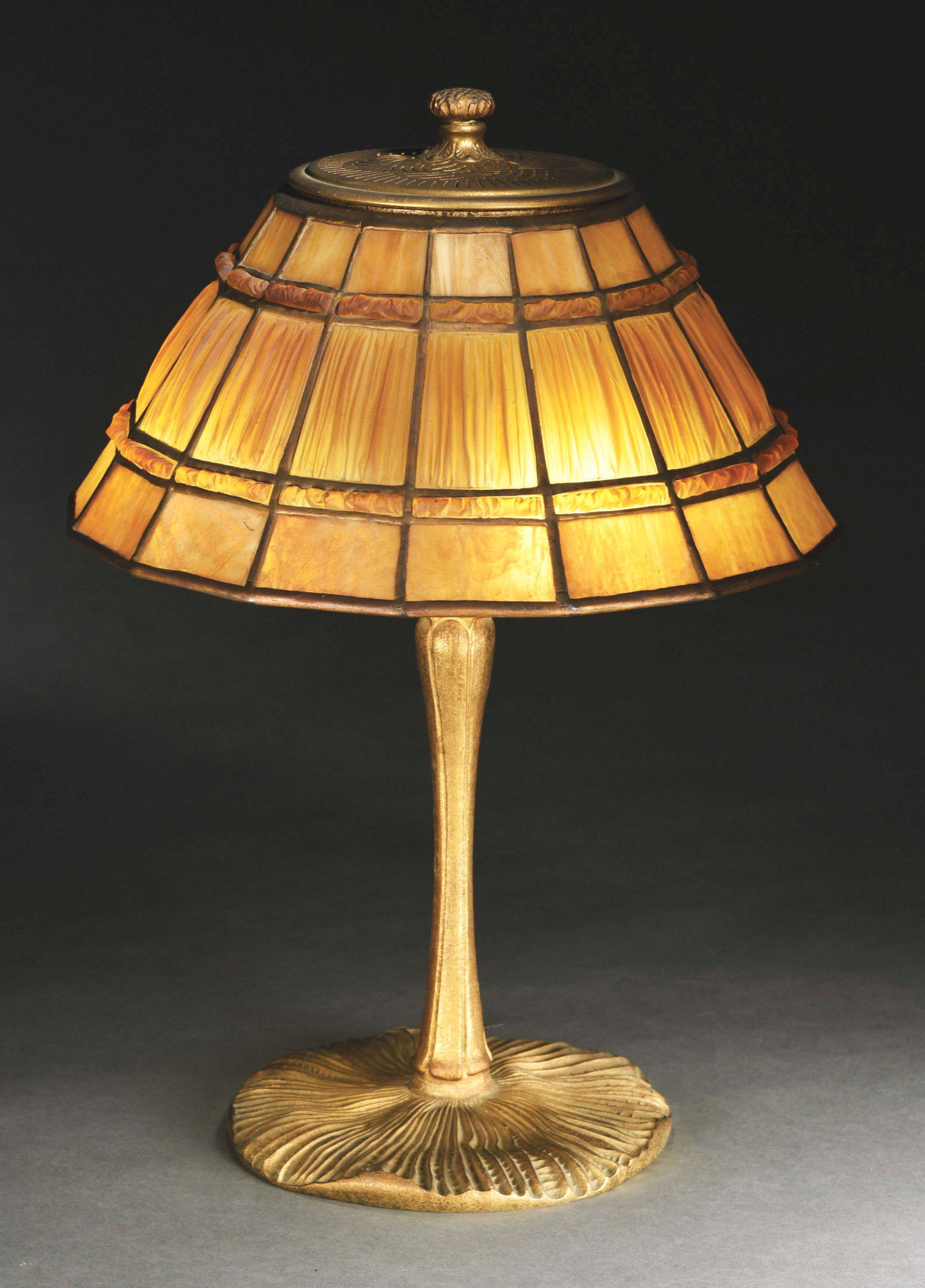 TIFFANY STUDIOS LINENFOLD DESK LAMP.: A linenfold shade on inverted mushroom base by Tiffany Studios. The 14” diameter shade features a large central band of tightly “folded” glass in rich tones of butterscotch. The linenfold glass 