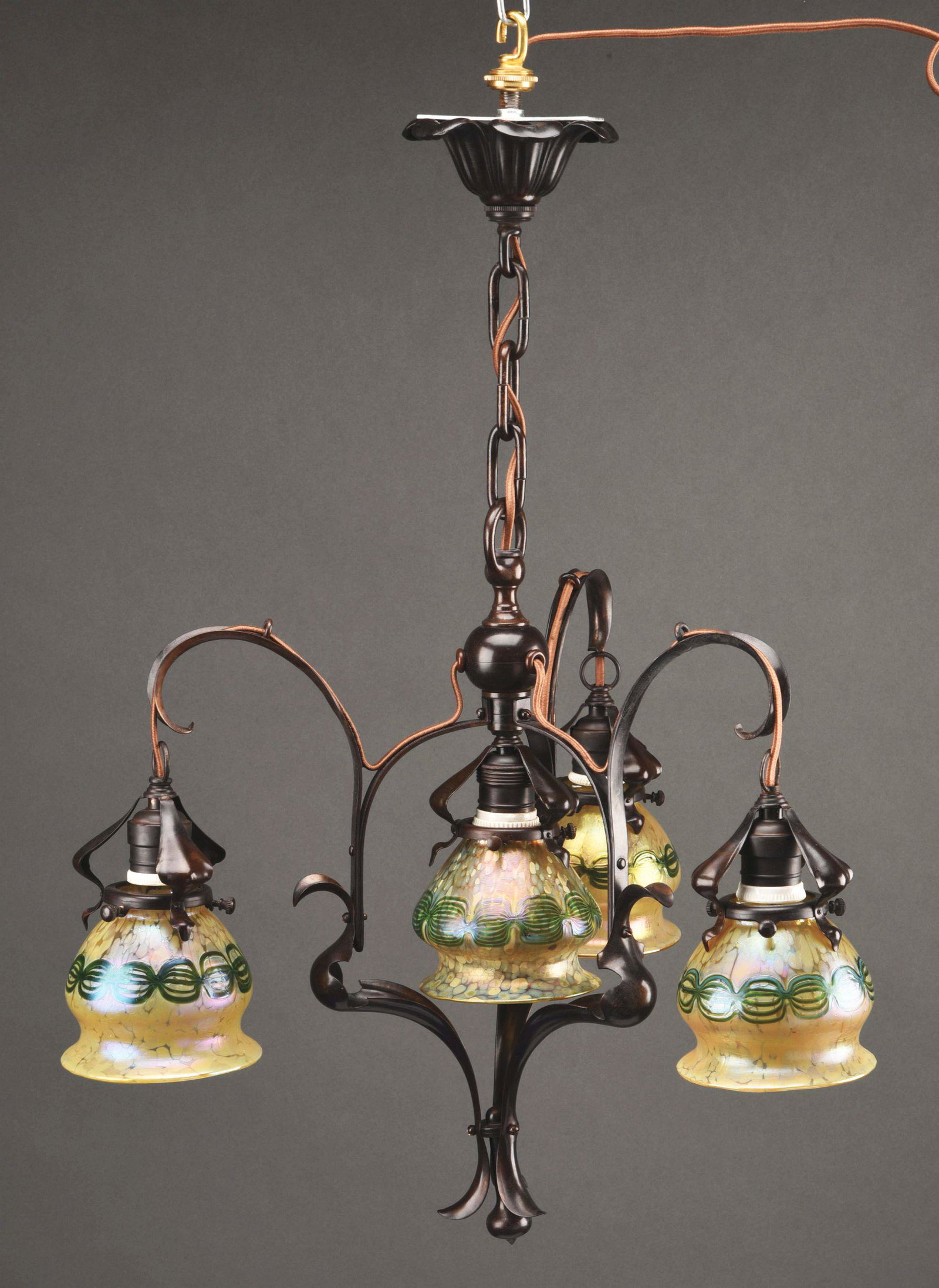 LOETZ CHANDELIER WITH FOUR SHADES.: An Art Nouveau patinated bronze and glass chandelier decorated with four matching Austrian art glass Loetz shades decorated with iridescent green chain-link against an iridescent oil spot background s