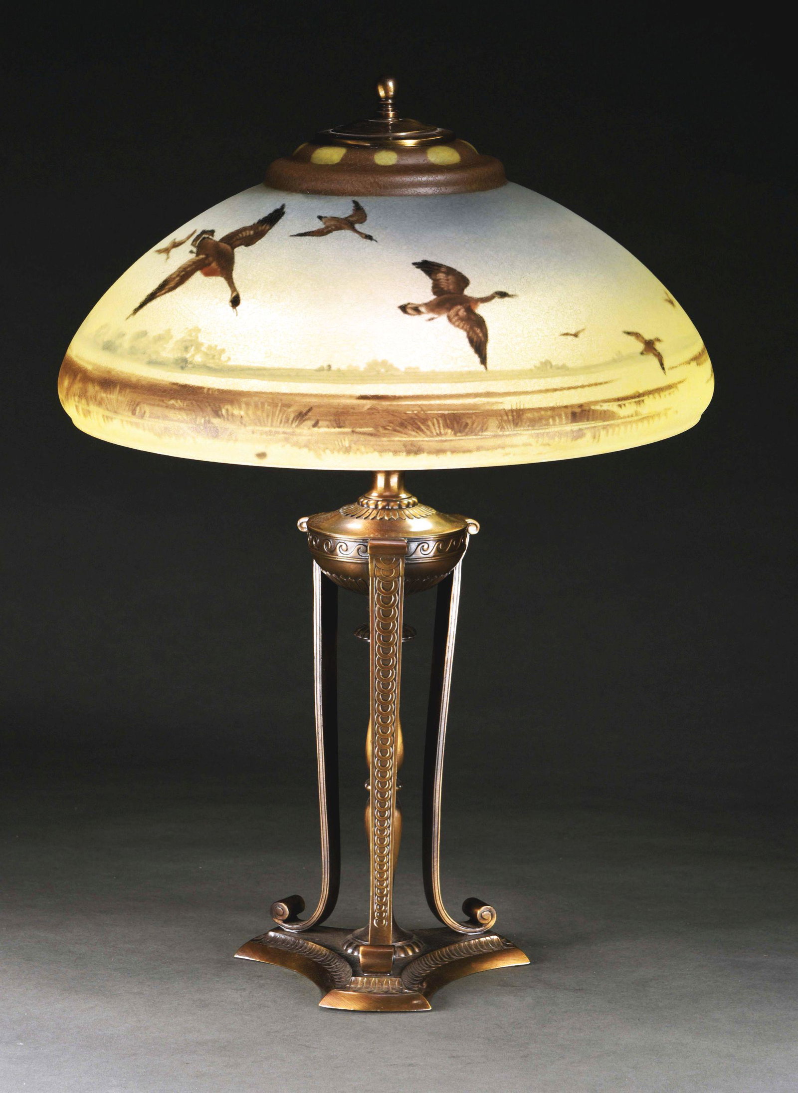 PAIRPOINT REVERSE PAINTED LAMP WITH GEESE IN FLIGHT.: A beautiful reverse painted lamp by Pairpoint. The shade depicts Canadian Geese in flight, over plains of grass. The geese are set against a background of blue sky, that progresses to yellow towards t