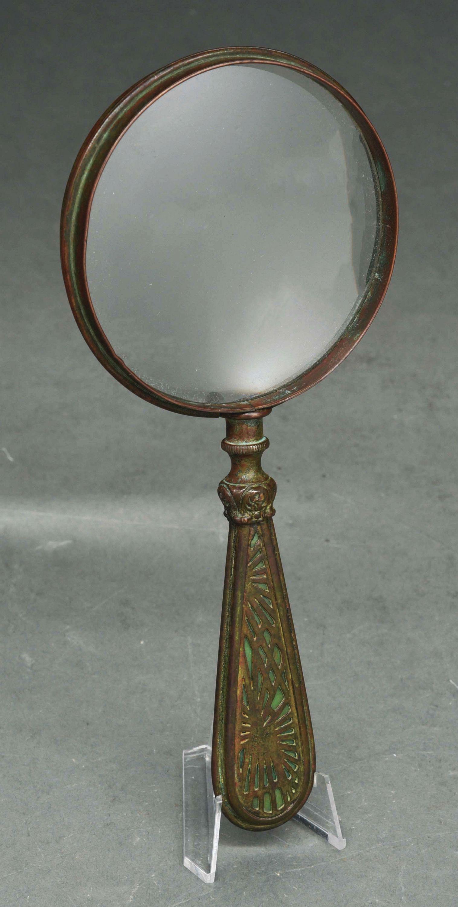 TIFFANY STUDIOS PINE NEEDLE MAGNIFYING GLASS.: A magnifying glass by Tiffany Studios, with green slag glass on handle, overlaid with patinated metal in pine needle pattern. Measuring 8” in length and is in excellent condition with no cracks, bre