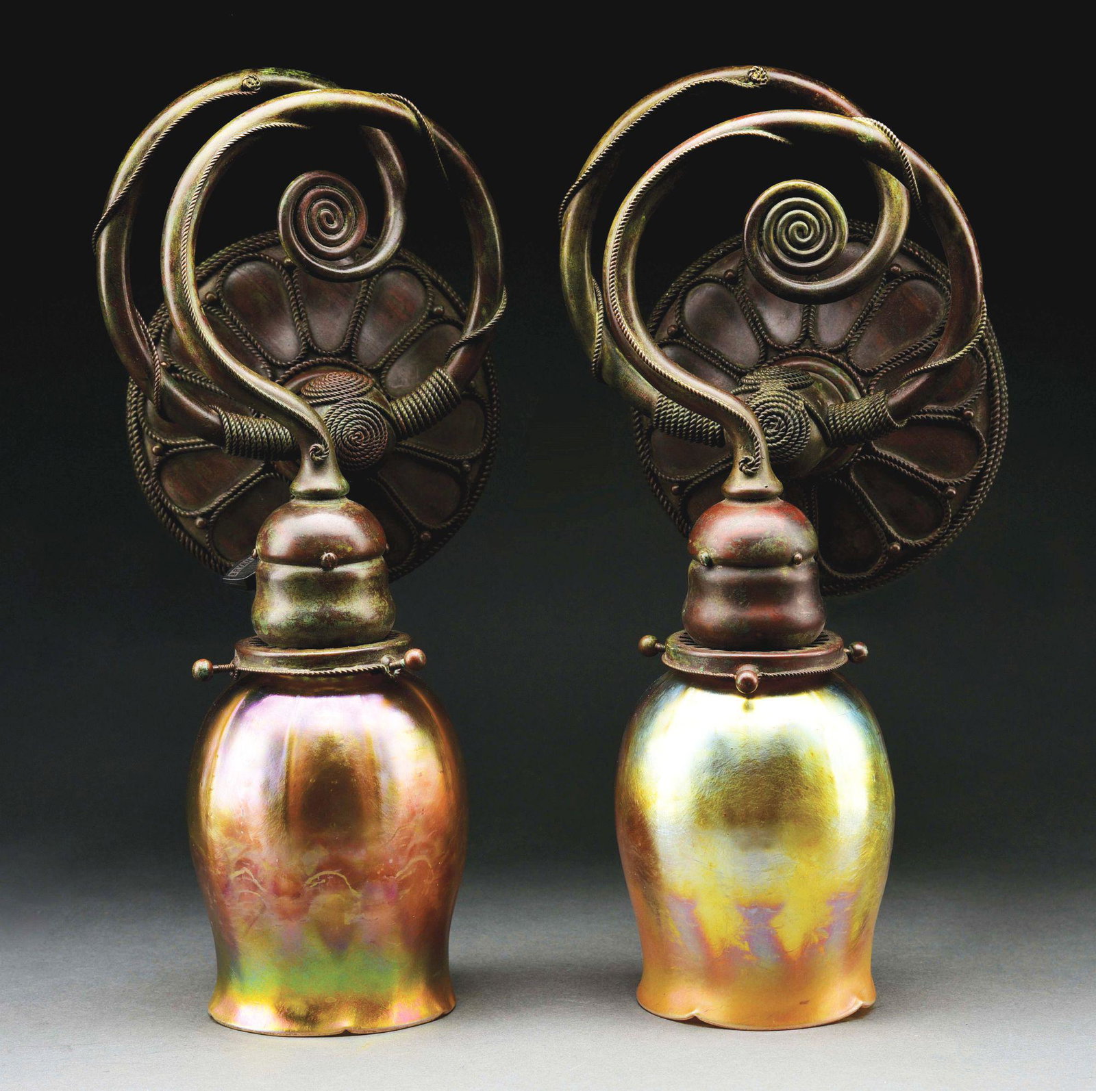 PAIR OF MOORISH DECORATED SCONCES.: A pair of Tiffany Studios Favrile glass and bronze single-light sconces, each with a circular backplate issuing the scrolling spiraling candle arms, the whole with applied twist wire work decoration t