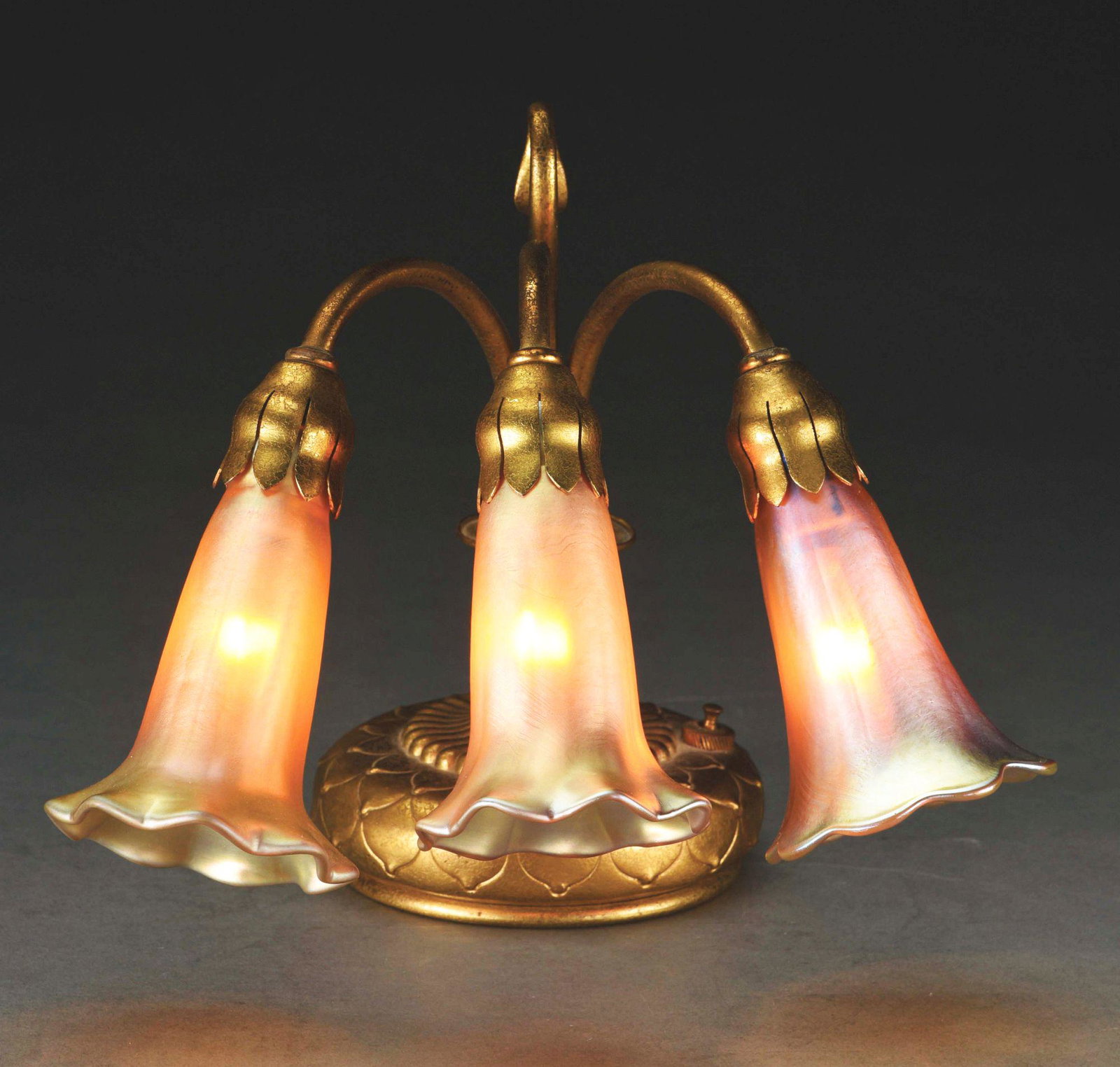 TIFFANY STUDIOS THREE-LIGHT LILY PIANO LAMP.: A lovely Tiffany Studios piano lamp with three art glass shades. The base is finished in a beautiful gold dore. It retains three white porcelain G.E. Co. sockets. It is properly signed to the undersid