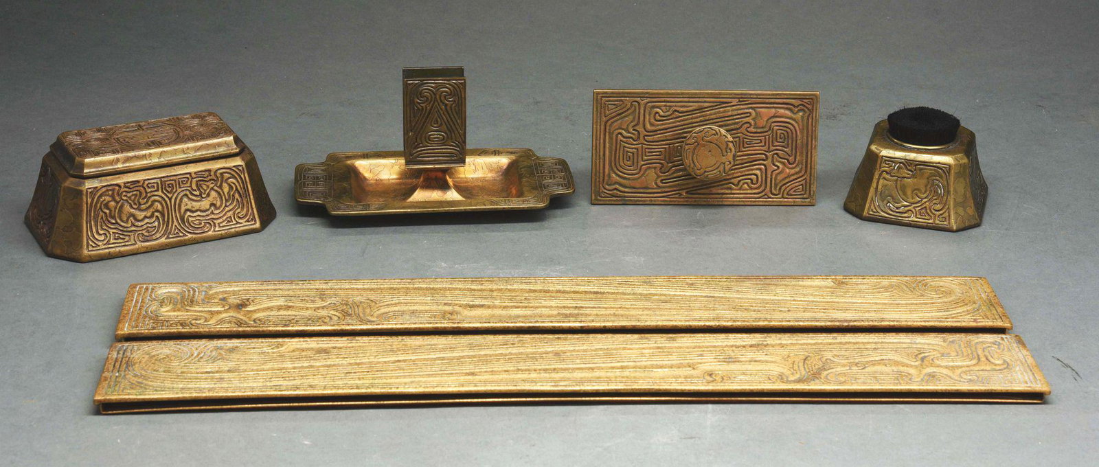 TIFFANY STUDIOS FIVE-PIECE DESK SET IN CHINESE PATTERN.: A beautiful five-piece desk set in the Chinese pattern in gold dore. Includes the following pieces: a pen brush holder (1772), rocker blotter (1760), matchbook holder (No visible number or signature),