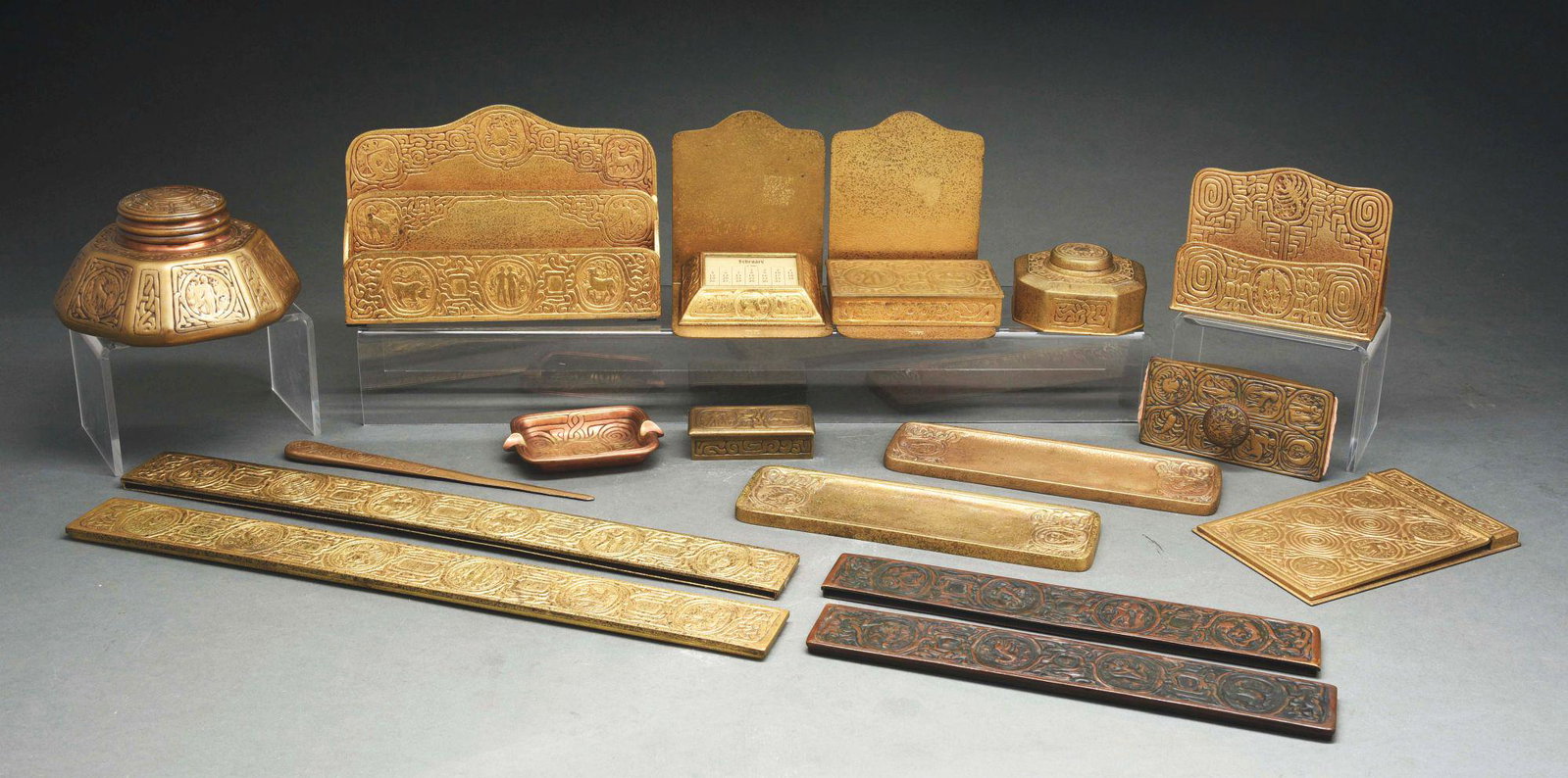 TIFFANY STUDIOS 15-PIECE DESK SET.: A 15-piece desk set with Zodiac pattern by Tiffany Studios in gold dore. Set includes: cigarette box (810), memo pad (1090), letter holder (1089), large inkwell with replaced non-fitting insert and no