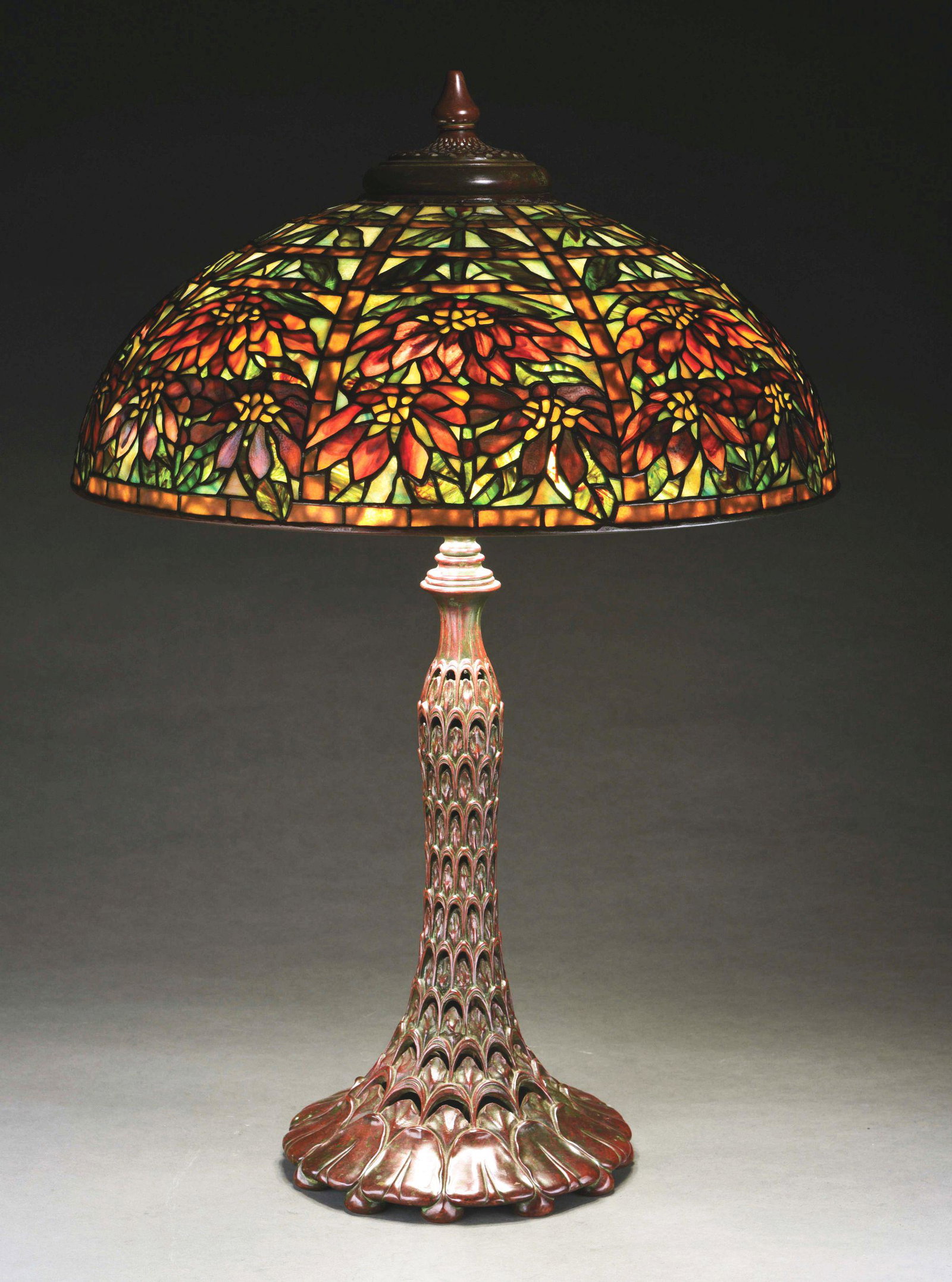 TIFFANY STUDIOS DOUBLE POINSETTIA LEADED GLASS LAMP: A gorgeous double poinsettia leaded glass lamp on a bronze arch and leaf base. While both shade and base are signed, we suspect both to be extraordinarily high quality, American reproductions, and are