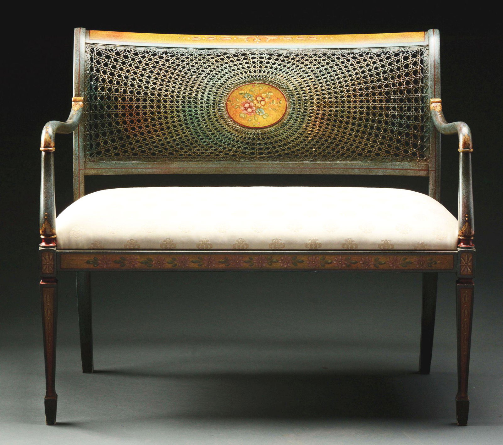 AN ATTRACTIVE ADAM'S STYLE DECORATED CANEBACK SETTEE.: 20th century. In blue-grey paint with "antiqued" surface, the crest and seat rails decorated with bellflowers and flower heads. The caned back centering an oval patera with floral spray. The shaped ar