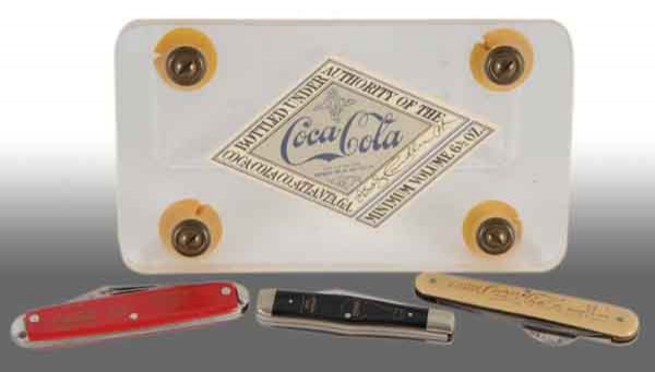 Lot of 4: Coca-Cola Items.: Description Includes three pocketknives and one reproduction diamond label. Only medium wear to two knives while the other two pieces have little to no wear. Condition (8.5, Excellent).