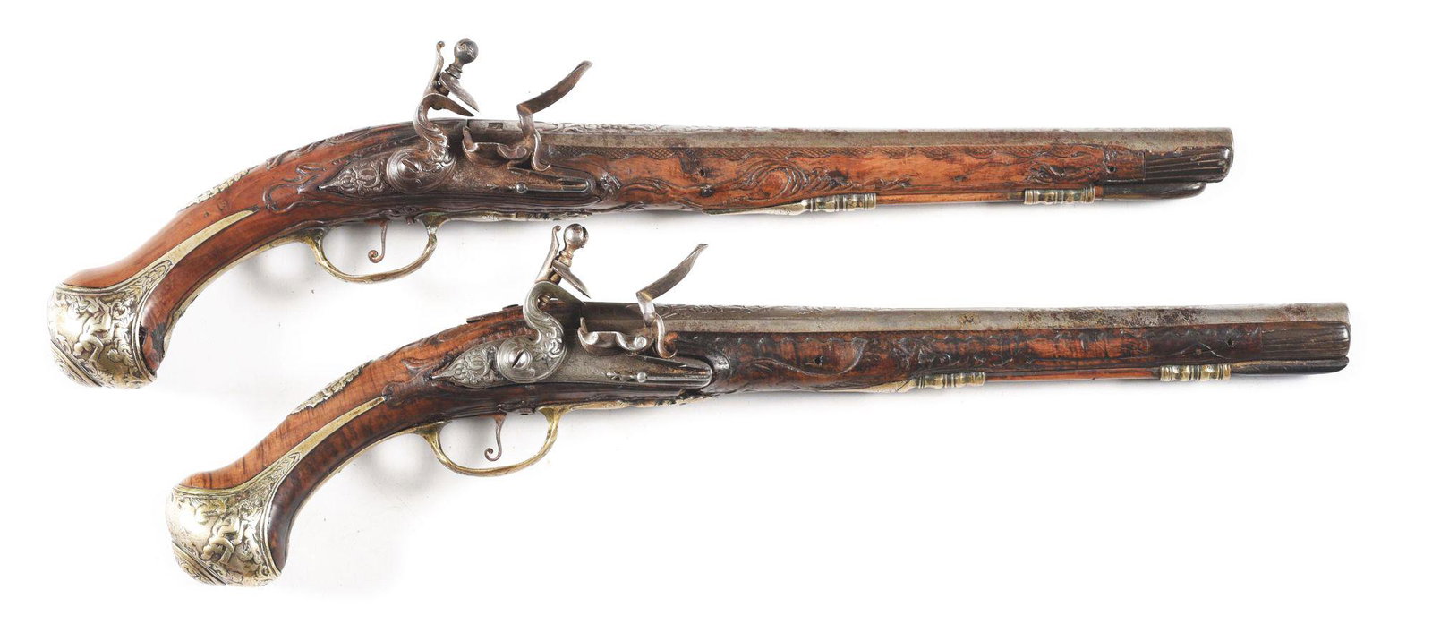 (A) PAIR OF LARGE AND DECORATIVE OTTOMAN FLINTLOCK: Both with chiseled and chased decorated iron barrels, each with 3 indistinct gold makers marks. Locks chiseled en suite and engraved with foliate scrolls. Fruitwood stocks are heavily carved with reli
