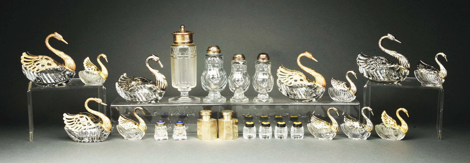A GROUP OF STERLING AND GLASS SWAN SALT CELLARS.: All with glass bodies and pierced sterling wings including four large and seven small and another; together with a glass and silver plate sugar caster; a set of three cut glass casters with facetted b