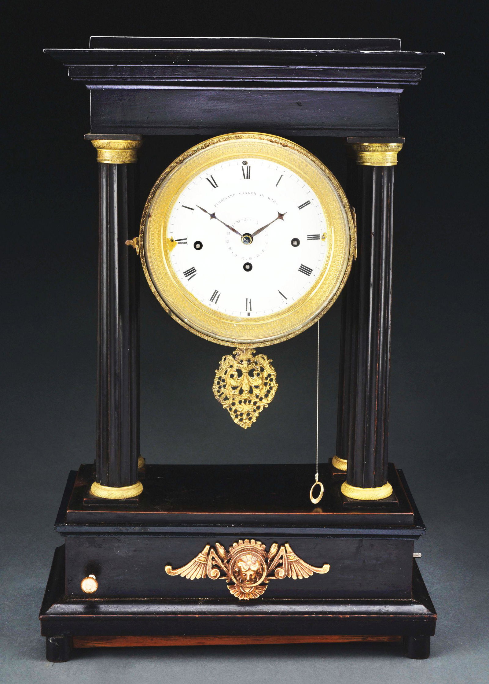 VIENNA PORTICO CLOCK WITH MUSIC BOX.: With a three train movement and a music box in the base. Ebonized and gilt case. Silk string suspension movement. The enamel dial signed: Ferdinand Vogler in Vien. Vienna, circa 1840. Music box plays 