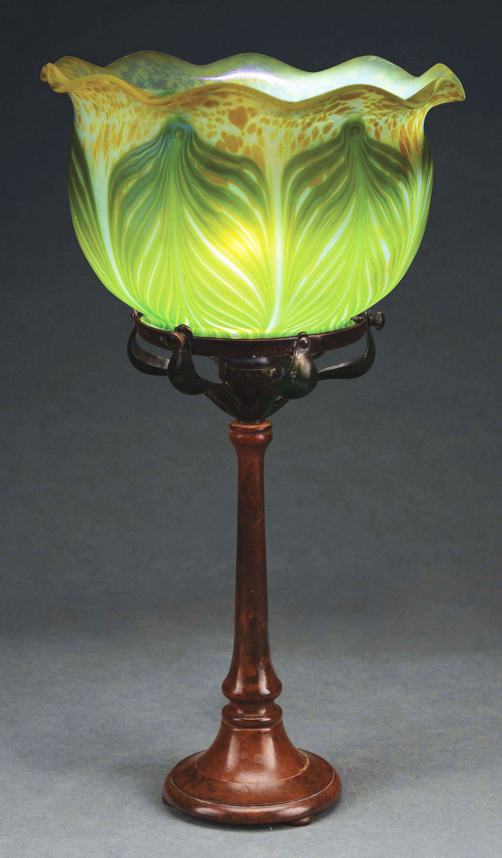 LOETZ DESK LAMP: An Austrian Art Nouveau patinated bronze and glass Loetz desk lamp, decorated with an oversized ruffled Loetz shade with iridescent blue-green large pulled feather decoration throughout against a yell