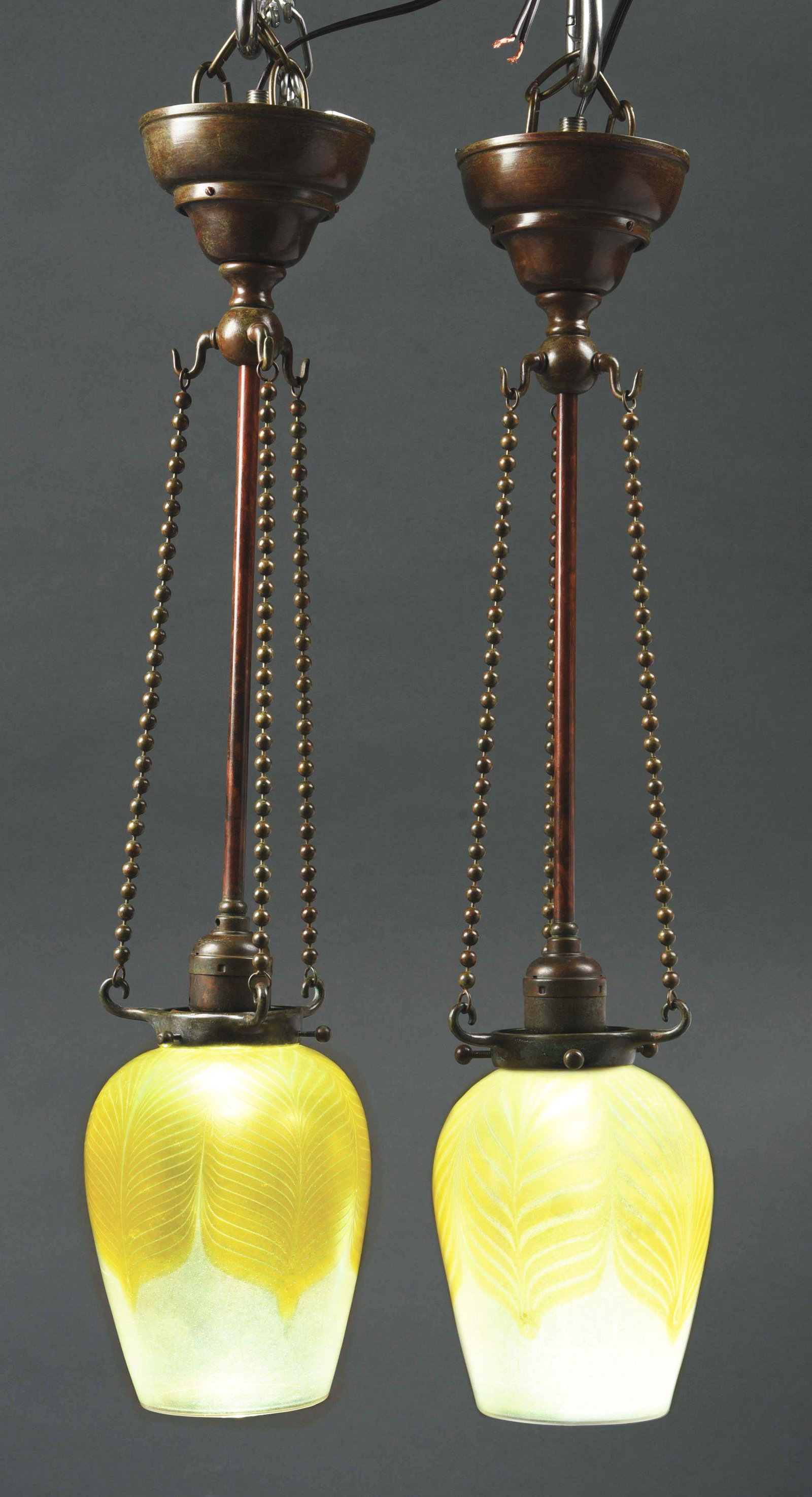 PAIR OF TIFFANY STUDIOS CHANDELIERS.: A pair of patinated bronze & favrile glass pendant/chandeliers by Tiffany Studios, each decorated with an oversized yellow pulled feather decoration against a yellow iridescent transparent background,