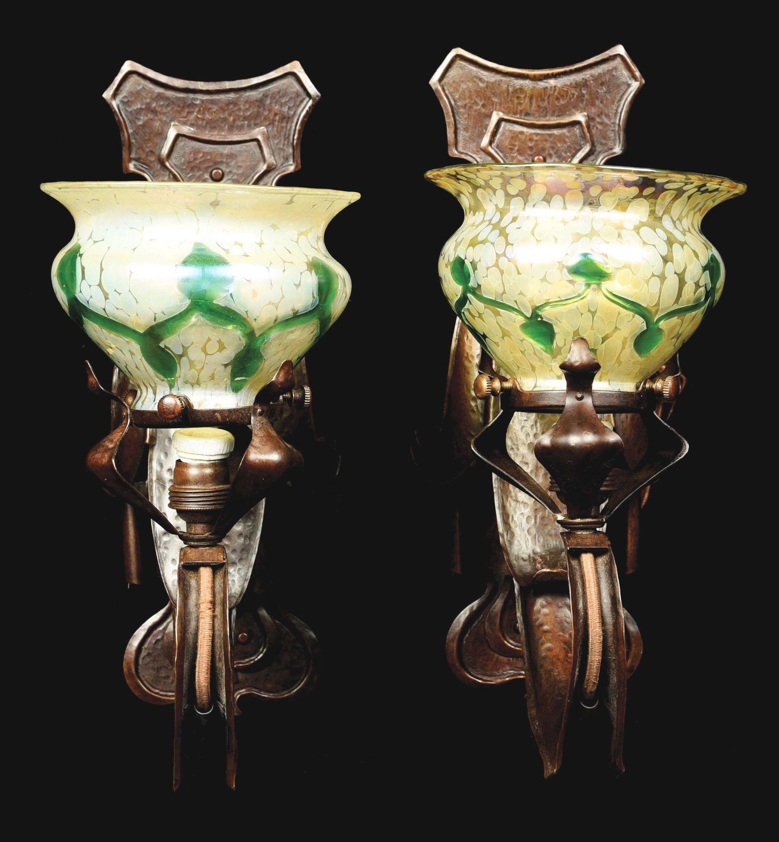 PAIR OF AUSTRIAN ART NOUVEAU SCONCES.: A pair of Austrian Art Nouveau patinated hammered copper fleur-de-lis sconces, each decorated with Austrian Loetz art glass, decorated with iridescent green leaf and vine decoration against an iridesc
