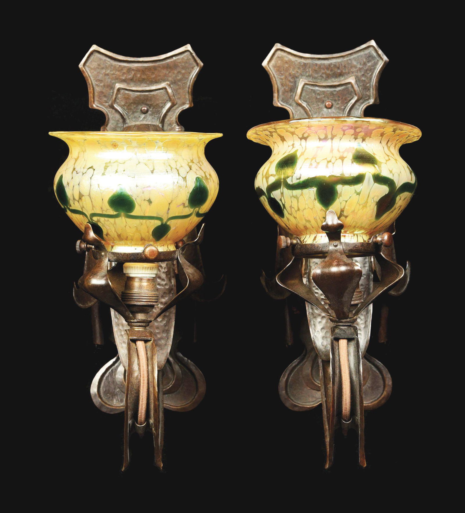 PAIR OF AUSTRIAN ART NOUVEAU SCONCES.: A pair of Austrian Art Nouveau patinated copper fleur-de-lis hammered copper sconces, each decorated with Austrian Loetz art glass decorated shades with iridescent green leaf and vine decoration again