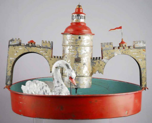 Tin Wind-Up Swan Pond Toy.: German. Working. When wound swan swims around under castle in tin tub. Moderate paint loss throughout and some repaint. 10" x 13".