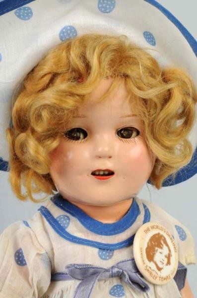 Composition Ideal Shirley Temple with Flirty Eyes: Original blonde mohair wig, crisp tagged dress with matching hat, original undies, reproduction button. Light crazing. Size: 13" T.