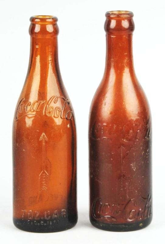 Lot of 2: Amber Coca-Cola Straight Sided Bottles.: Description 1903 to 1916. Both with a vertical arrow on either side. One Knoxville, TN and one Cleveland, OH. Medium overall wear. Condition (Very Good). Size Each: 8" T.
