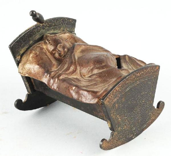 Cast Iron Baby in Cradle Still Bank.: Description With rosettes on side of bed. Provenance: From the Whiting Collection. Condition (Excellent Plus). Size 4" L.