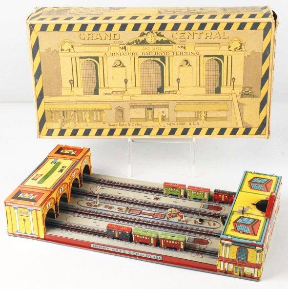 Tin Henry Katz Grand Central Station Wind-Up Toy.: Working. Nice color lithography of trains going in and out of station. Appears to be complete with four tracks. Some scratching, denting, and fading to roofs. Includes original box with some creasing,