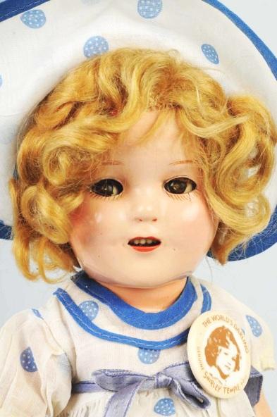 Composition Ideal Shirley Temple with Flirty Eyes: Original blonde mohair wig, crisp tagged dress with matching hat, original undies, reproduction button. Light crazing. Size: 13" T.