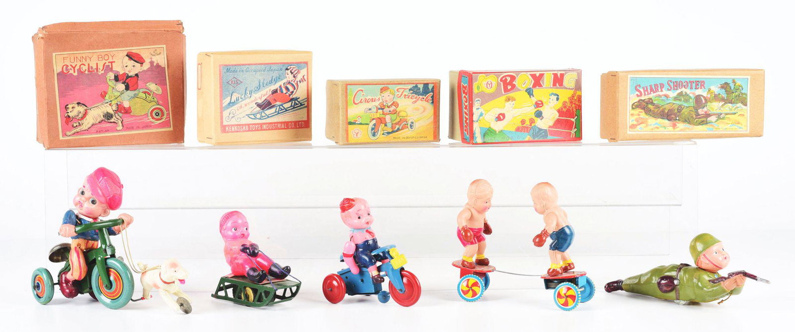 LOT OF 5: PRE-WAR OCCUPIED AND POST-WAR JAPANESE: All in original boxes. Pre-war Funny Boy cyclist, shows boy on cycle being followed by dog; nice, colorful paper label. Occupied Japanese Lucky Sledge. Occupied Japanese Sharp Shooter; military figure