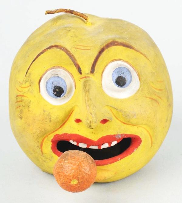 Apple Head with Bobbling Tongue Candy Container.: Intricately detailed papier mache head with large protruding hook nose, goofy eyes, and open mouth with a spring bobbling orange protruding from chicklet teeth. Lacking enclosure on underside. Size: 3